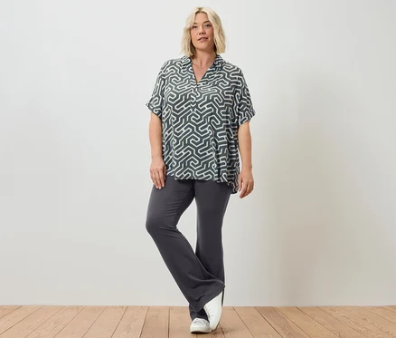 Eine Frau posiert in ausgestellten Leggings und einer bedruckten Bluse.