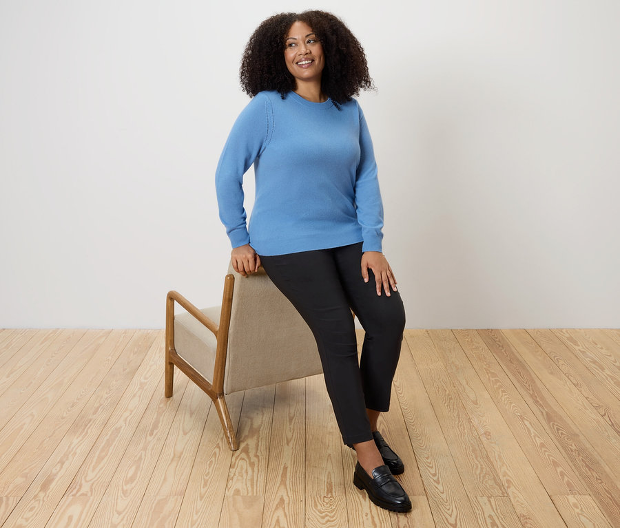 Frau sitzt auf einem Stuhl und trägt einen blauen Feinstrickpullover mit Cashmere.