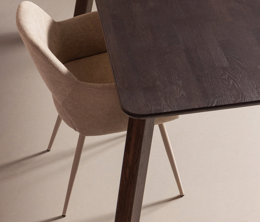 Detailaufnahme eines naturfarbenen Woood »Jenny« Stuhls aus einem 2er-Set neben einem dunklen Holztisch.