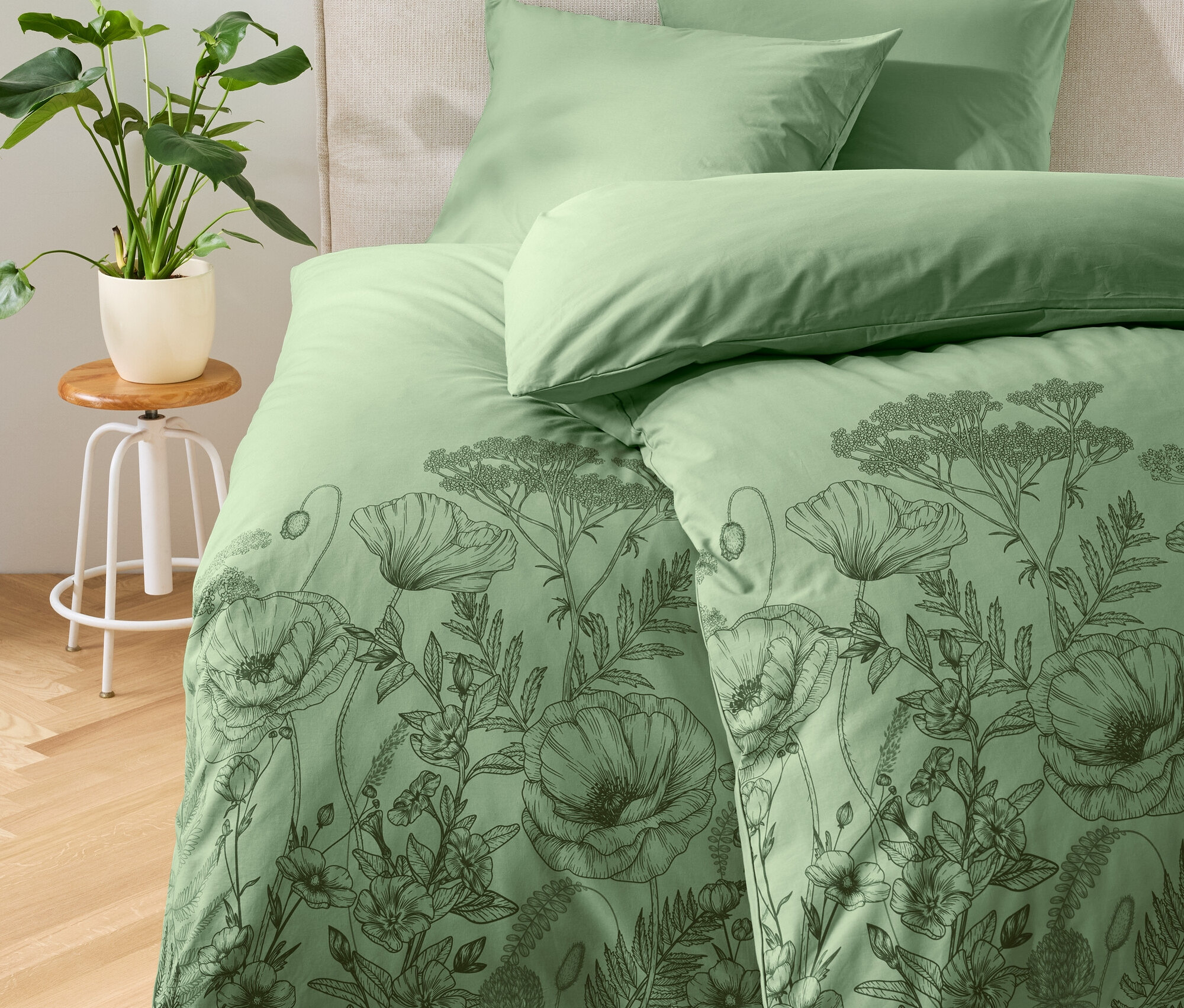 Grüne Bettwäsche mit Blumenmuster auf einem Bett.