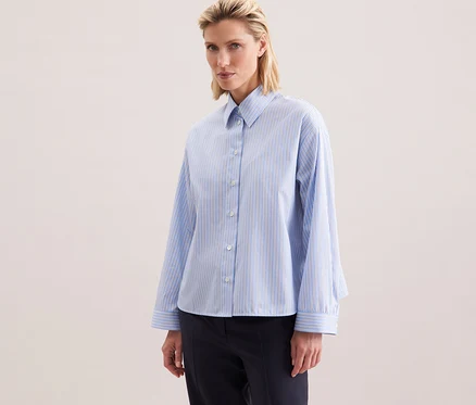 Frau trägt eine Seidensticker Oversize-Hemdbluse mit blauen Streifen.