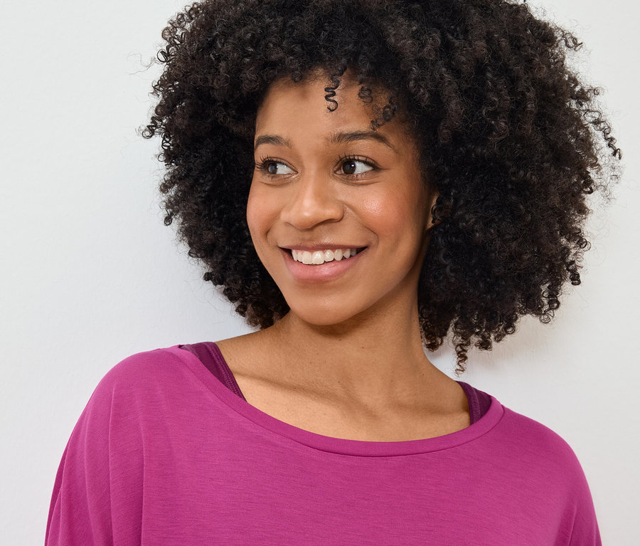 Porträt einer lächelnden Frau mit Afro-Frisur in einem pinkfarbenen T-Shirt.