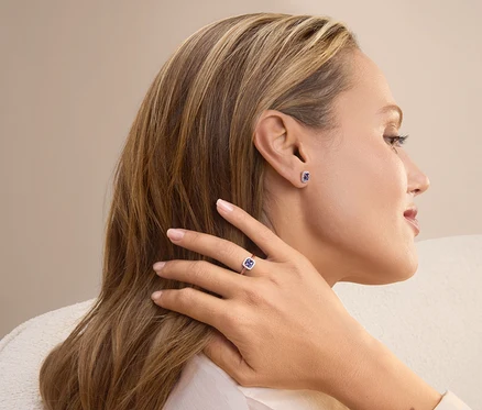 Profil einer blonden Frau, die einen Ring und Ohrringe mit blauen Steinen trägt.