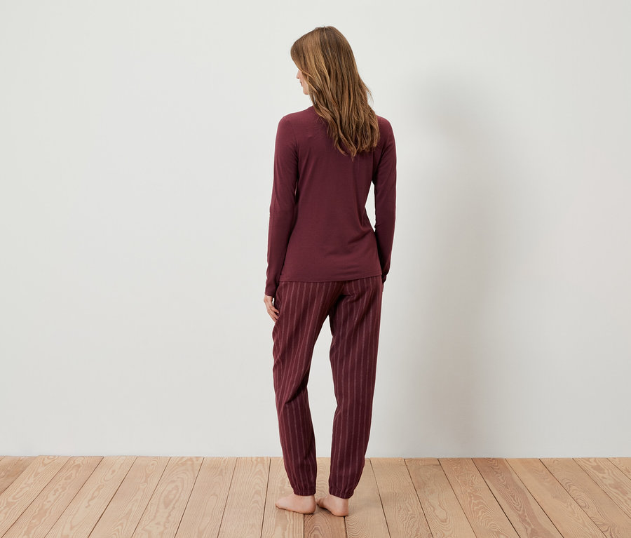 Frau steht mit dem Rücken zur Kamera und trägt einen bordeauxfarbenen Schlafanzug.