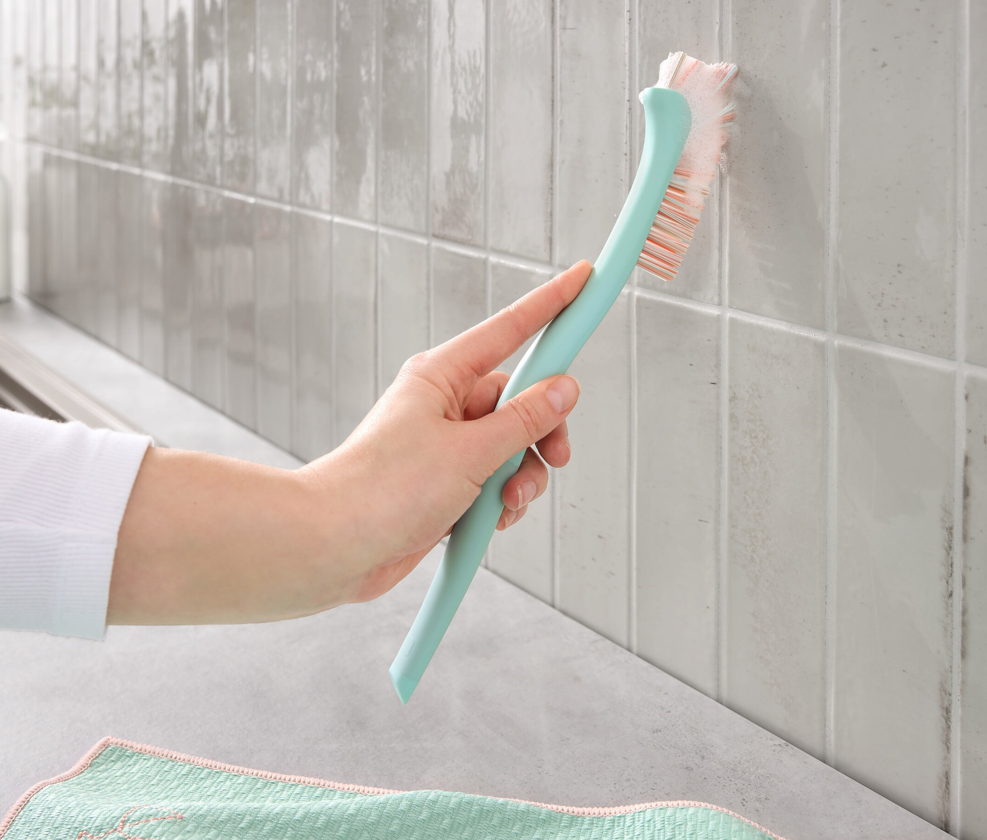 Eine Hand reinigt mit einer Fugenbürste schmutzige Fugen auf Fliesen.