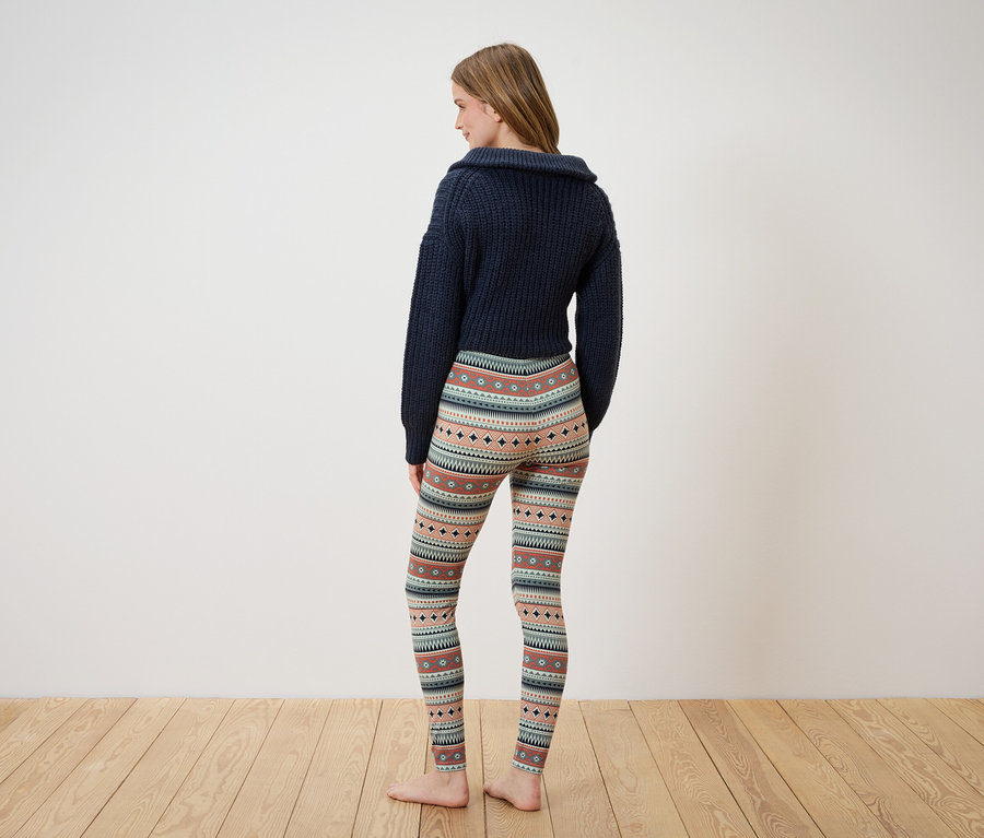 Frau mit dunkelblauem Pullover und gemusterten Leggings steht mit dem Rücken zur Kamera.