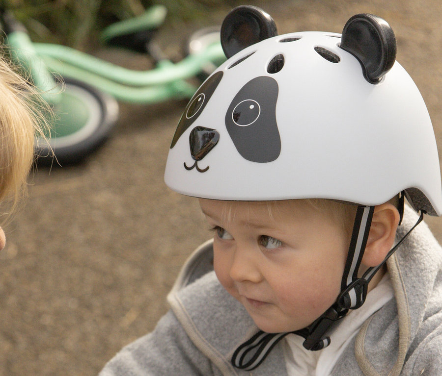 Mutter knöpft einem kleinen Jungen mit einem HUDORA Kinderhelm »Pandy« auf dem Kopf die Jacke zu.
