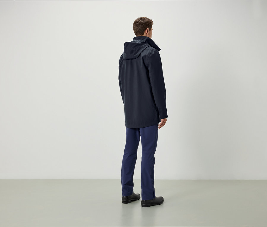 Mann von hinten, trägt eine blaue Jacke mit Kapuze, blaue Hose und schwarze Schuhe.