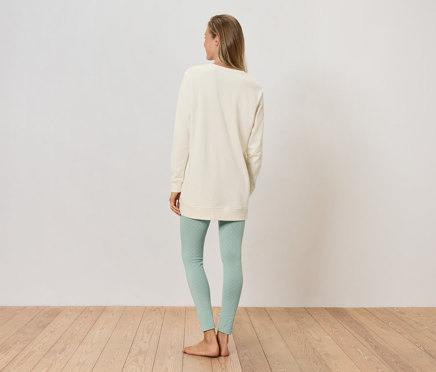 Frau steht mit dem Rücken zur Kamera, trägt ein cremefarbenes Sweatshirt und hellgrüne Leggings.