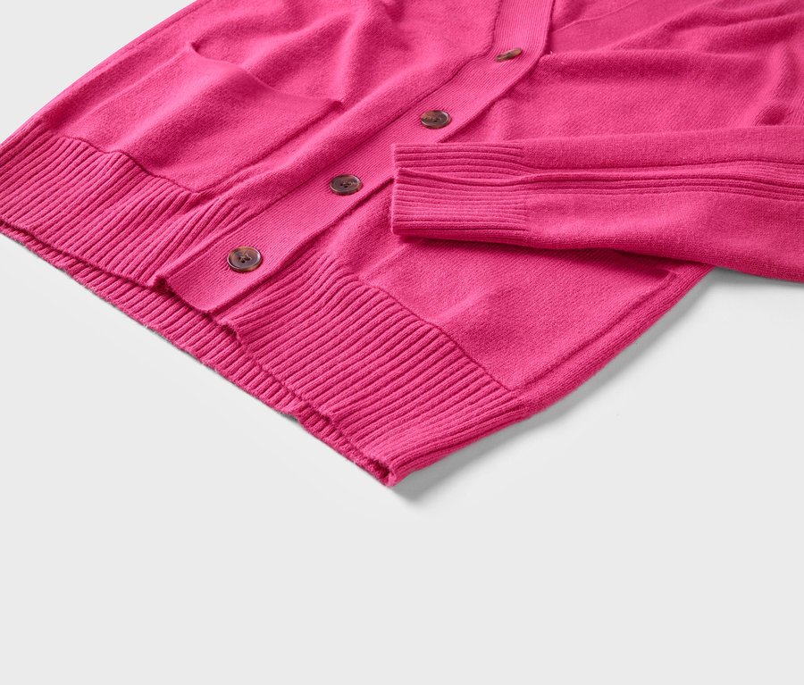 Detailaufnahme einer pinken Strickjacke mit Knöpfen und einer Tasche.