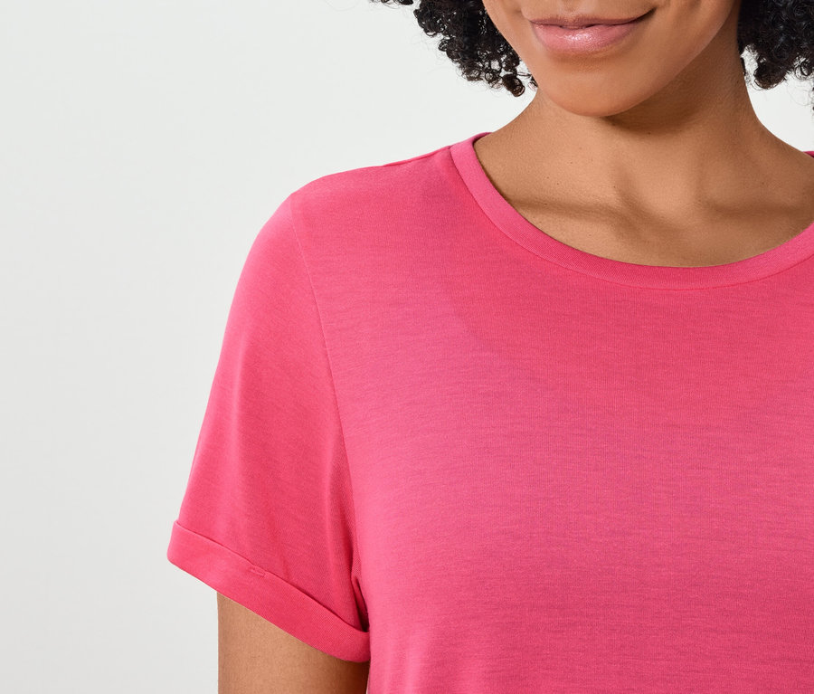 Oberkörper einer Frau mit dunklen Haaren in einem rosa Kurzarm-T-Shirt.