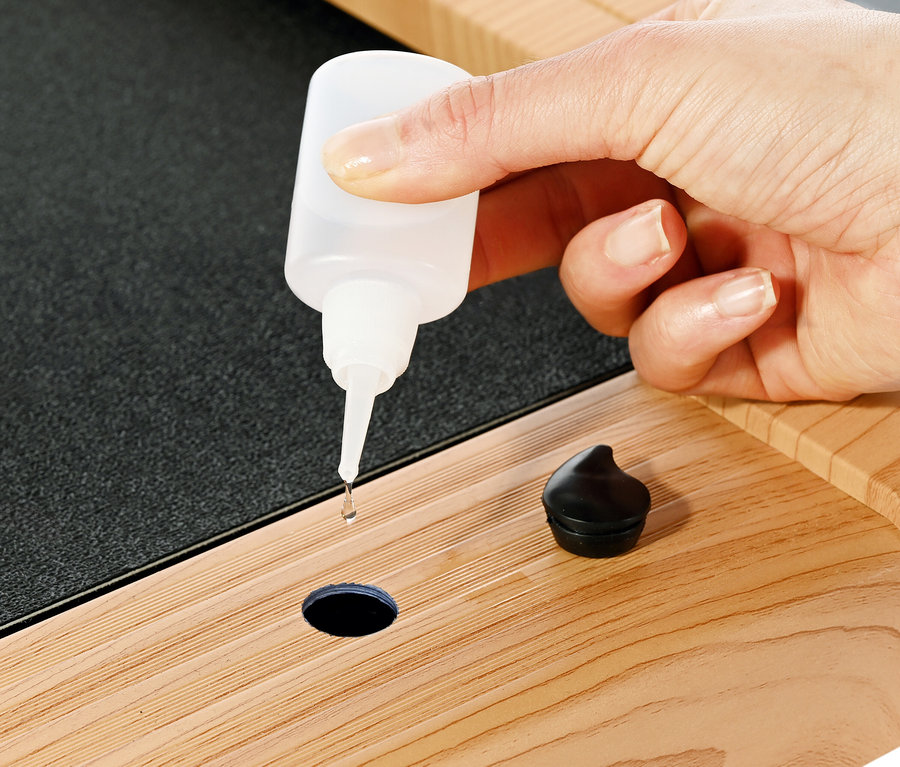 Eine Hand träufelt Öl aus einer Flasche in ein Loch auf einem Walking-Pad »4.2 Holzoptik«.