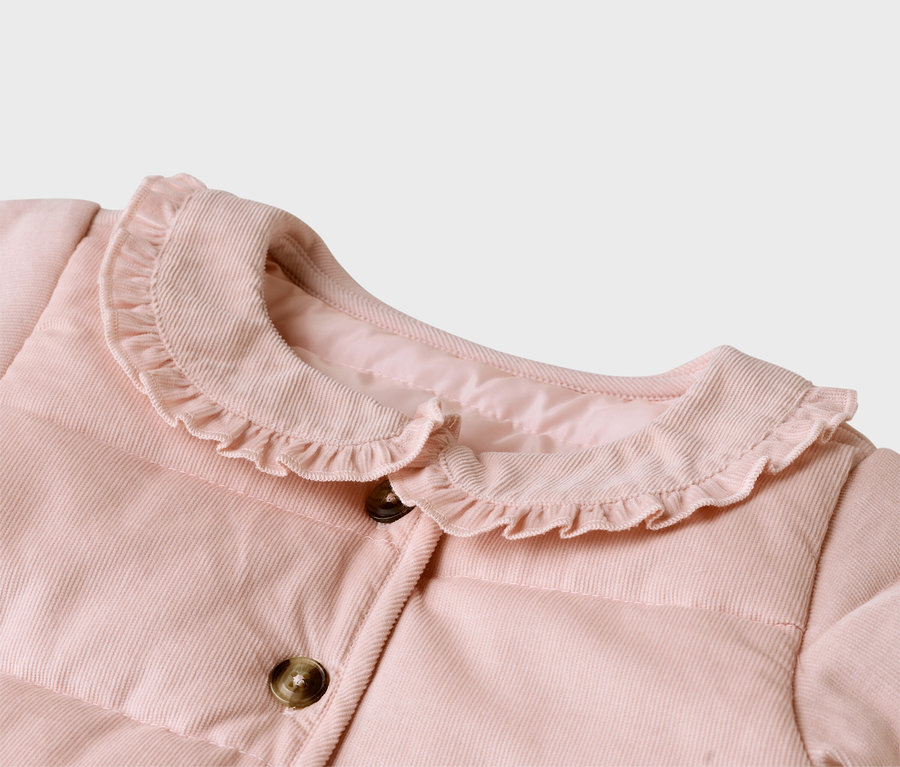 Nahaufnahme einer rosa Cordjacke mit Rüschenkragen und braunen Knöpfen.