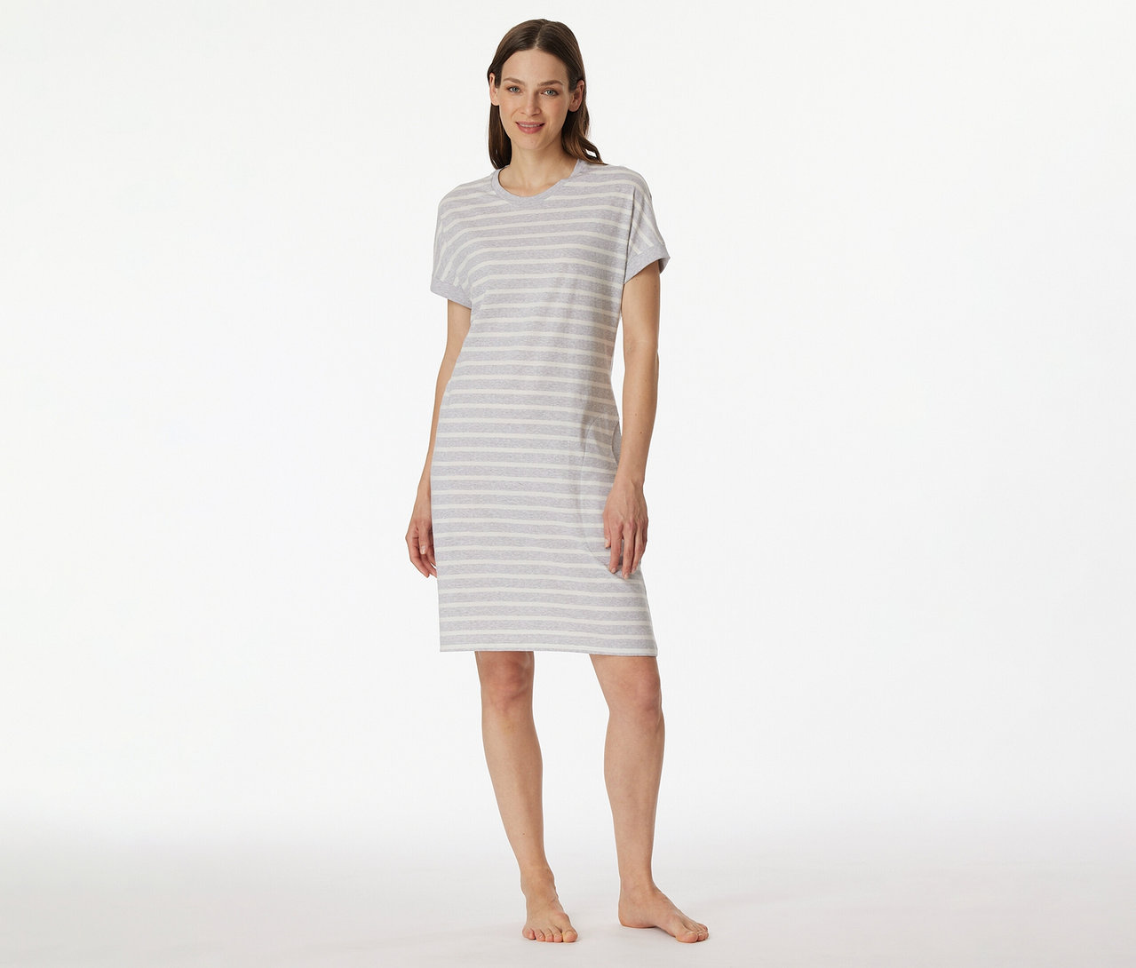 Frau in SCHIESSER Kurzarm-Sleepshirt mit grau-weißen Streifen, barfuß vor weißem Hintergrund.