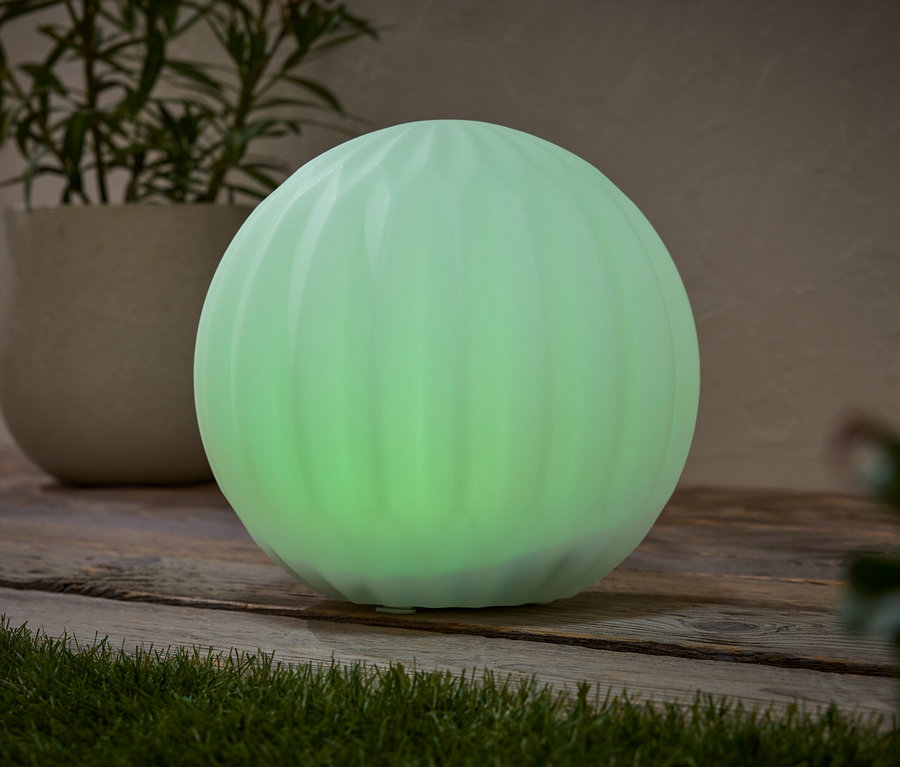 Eine grüne kugelförmige Lampe steht auf einer Holzoberfläche, neben einer Topfpflanze.