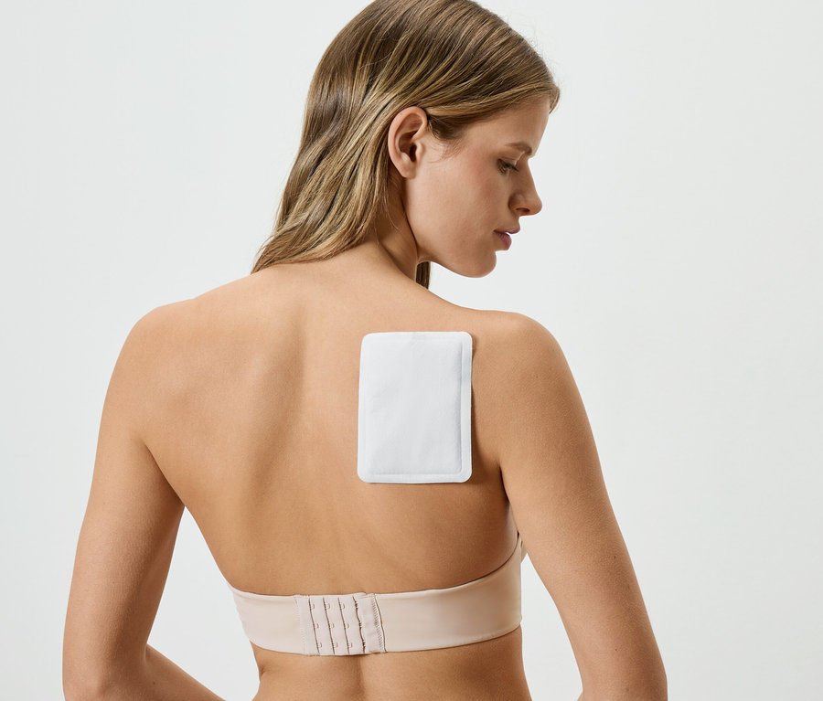 Frau mit Wärmepflaster am Rücken, trägt einen hautfarbenen BH.