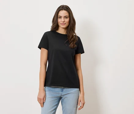 Frau mit gewelltem Haar trägt ein schwarzes T-Shirt und Jeans.