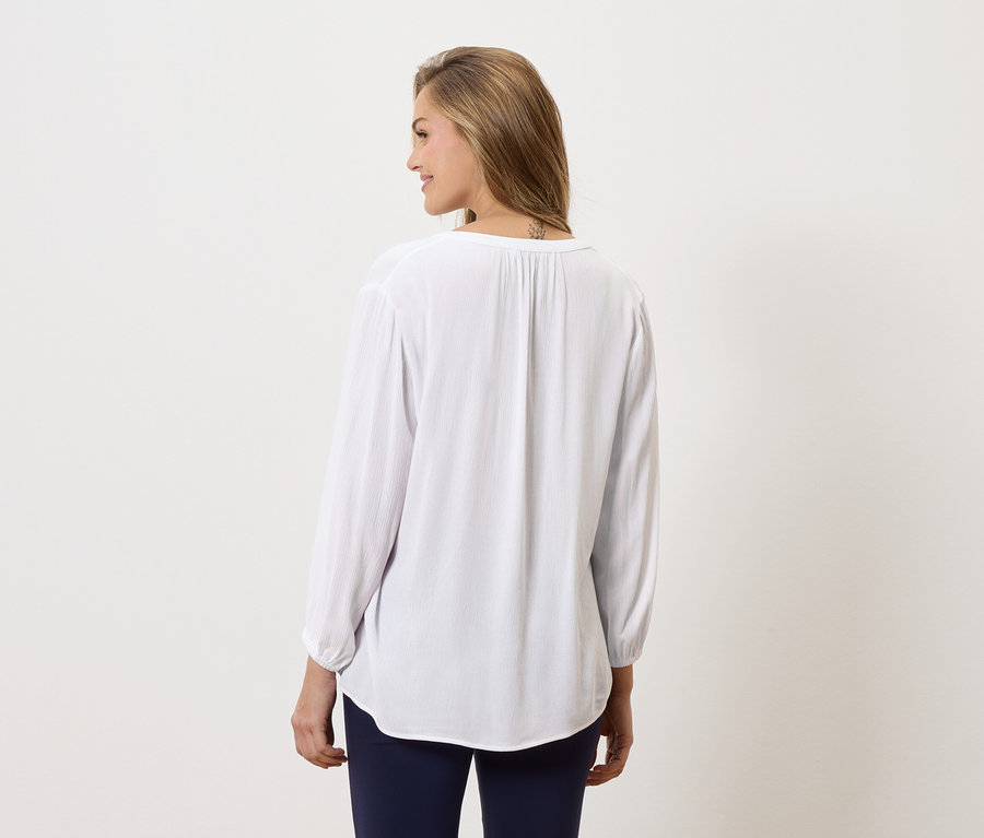 Frau von hinten, trägt eine lange, weiße Bluse und blaue Hosen.