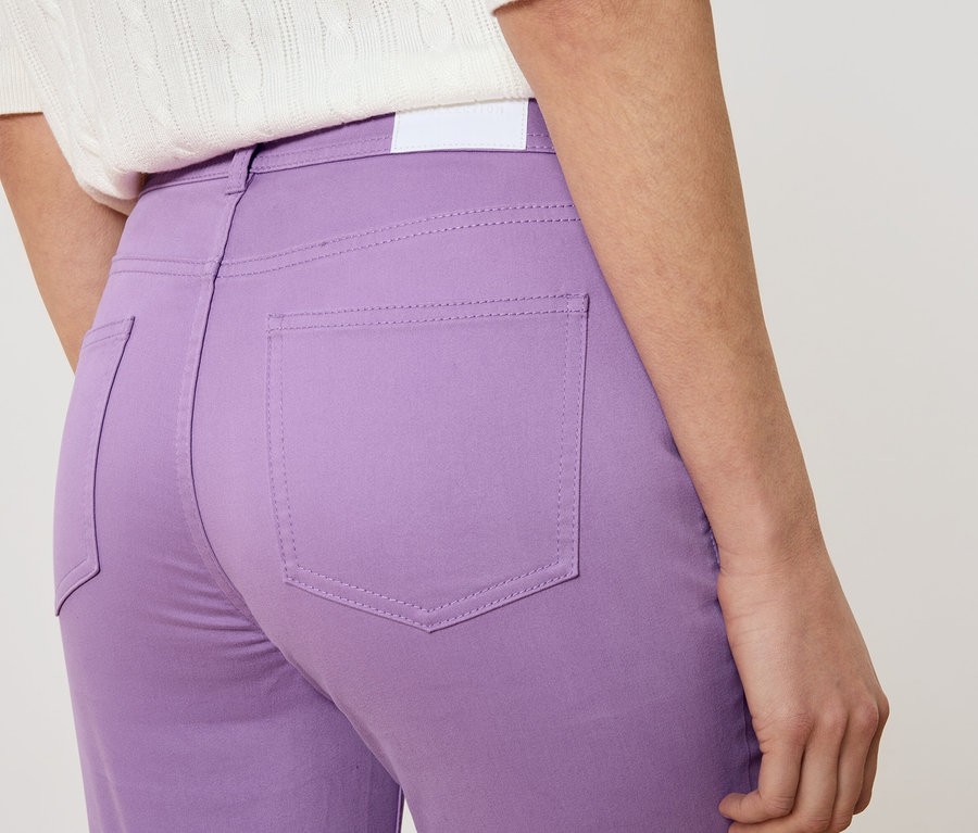 Nahaufnahme einer Frau von hinten, die eine violette Hose und ein weißes Oberteil trägt.
