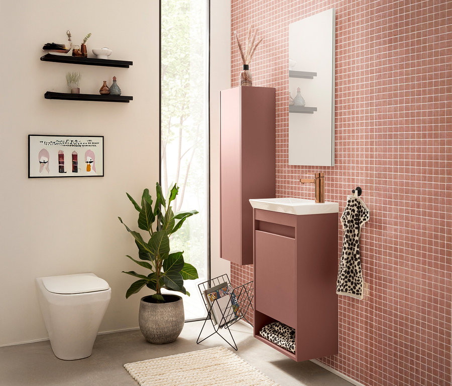 Ein Badezimmer mit einer Toilette, einem Waschtisch mit Unterschrank und einem Spiegelschrank an einer rosa gefliesten Wand.