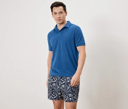 Mann trägt ein blaues Poloshirt und gemusterte Badeshorts.