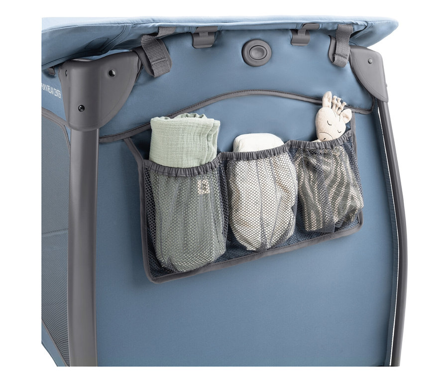 Ein blaues Kinderbett mit drei Netztaschen, in denen eine grüne Decke, Windeln und ein Stofftier liegen.