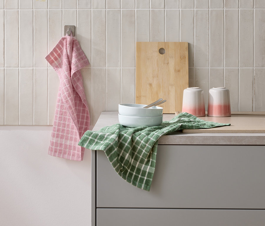 Auf einer Küchentheke stehen zwei Schalen mit Besteck, zwei Becher und ein Schneidebrett. Ein rosa und ein grünes Geschirrtuch liegen daneben.