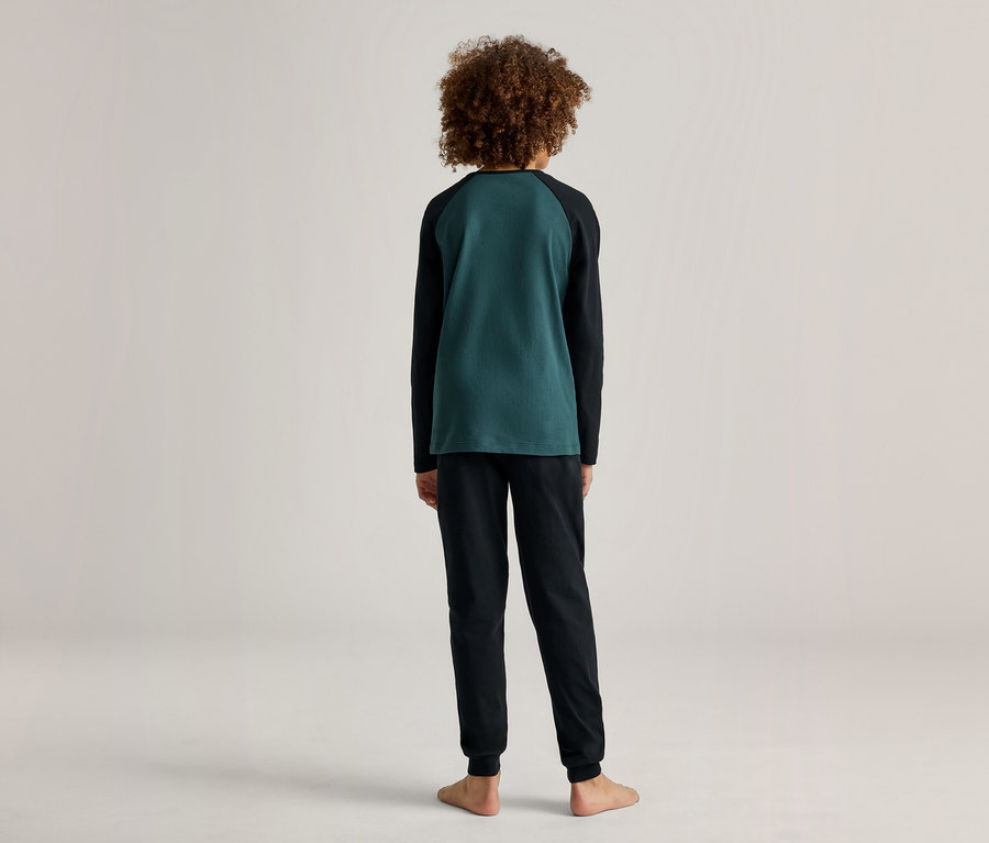 Rückansicht eines barfüßigen Kindes mit lockigem Haar, das einen grün-schwarzen Pyjama trägt.