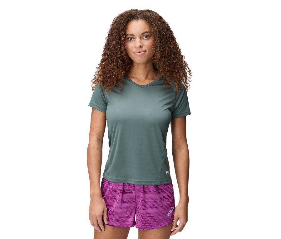 Frau mit lockigem Haar trägt ein graues T-Shirt und pinke Shorts.