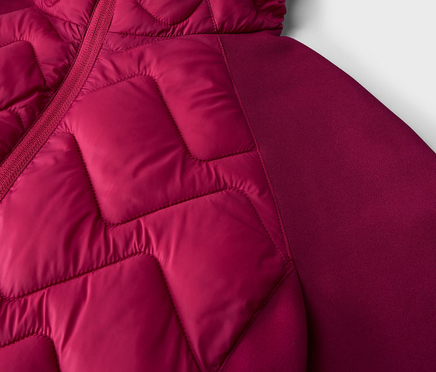 Nahaufnahme einer magentafarbenen Jacke mit gesteppter Vorderseite in geometrischem Muster und glattem Ärmel/Seitenbereich, mit sichtbarem Reißverschluss.