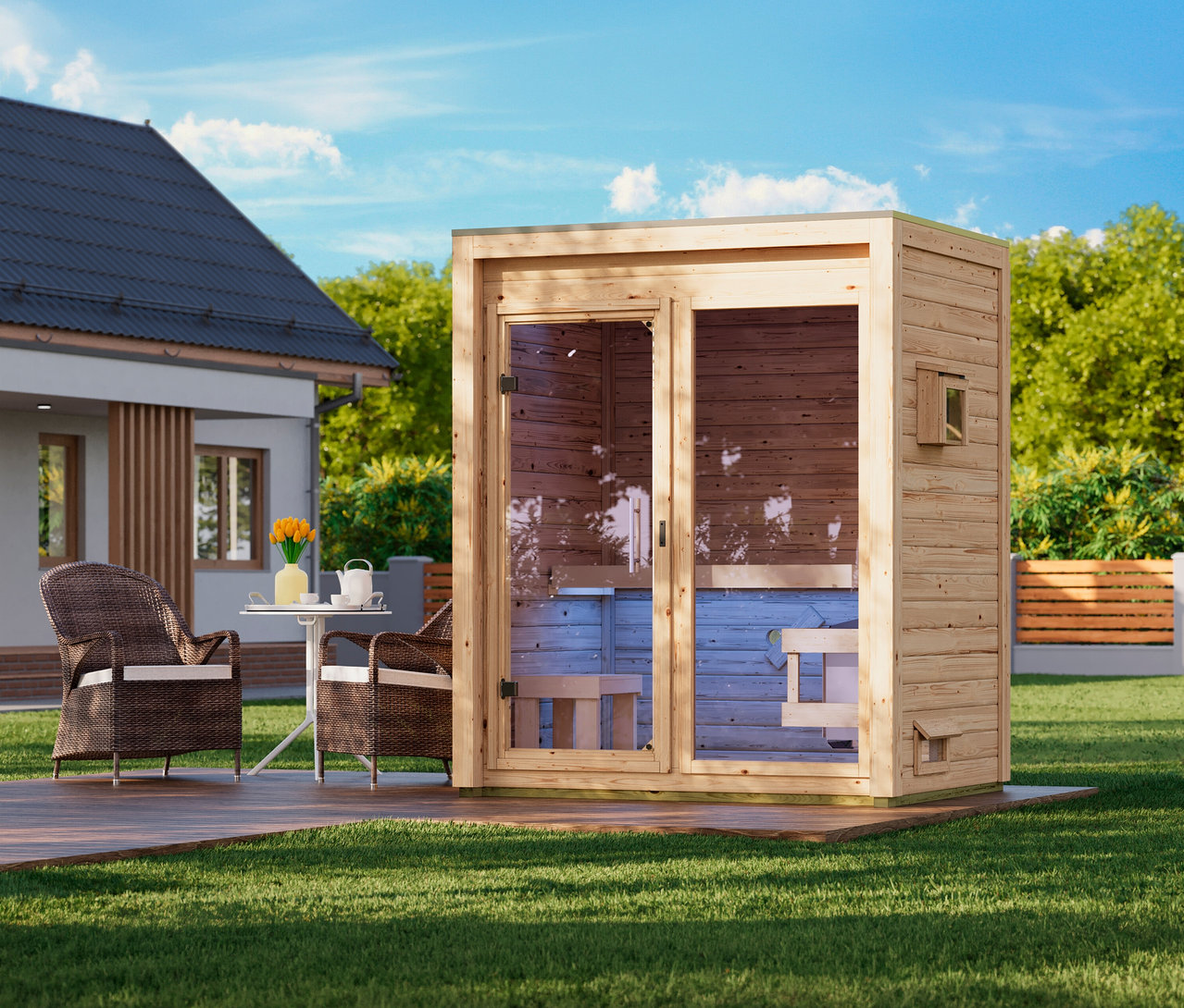 Eine hölzerne Außensaunakabine mit Glastüren steht auf einer Holzterrasse in einem grünen Garten. Daneben stehen zwei Korbsessel mit weißen Kissen und ein kleiner weißer Tisch mit gelben Blumen. Im Hintergrund sind ein Haus und Bäume unter blauem Himmel zu sehen.