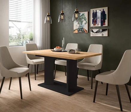 Esstisch mit Holzplatte und schwarzem Fuß, umgeben von vier hellen Stühlen. Dunkelgrüne Wand mit drei Bildern, Holzfußboden und Fenster mit Jalousien. Auf dem Tisch stehen eine Obstschale, Kerzen und Geschirr.