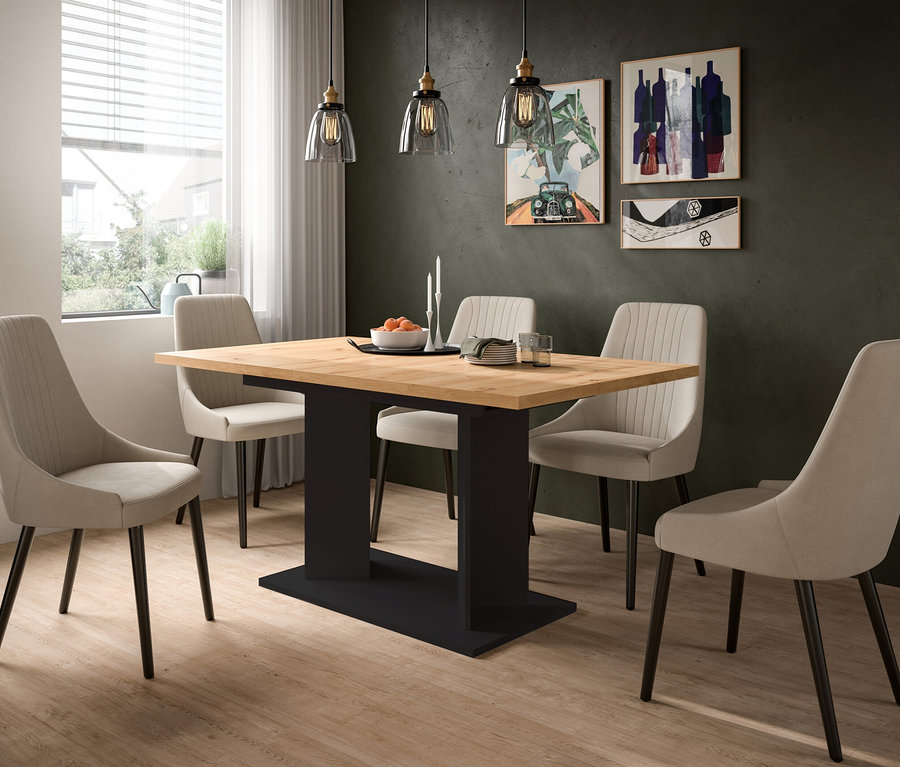 Esstisch mit Holzplatte und schwarzem Fuß, umgeben von vier hellen Stühlen. Dunkelgrüne Wand mit drei Bildern, Holzfußboden und Fenster mit Jalousien. Auf dem Tisch stehen eine Obstschale, Kerzen und Geschirr.