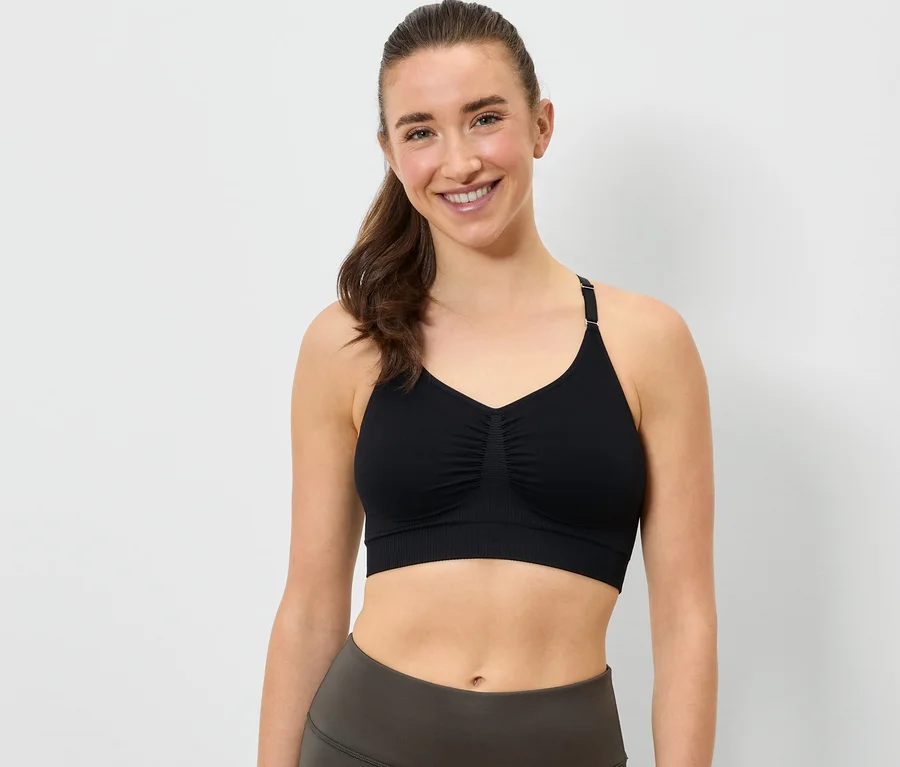 Lächelnde Frau trägt einen schwarzen Sport-BH und graue Leggings.