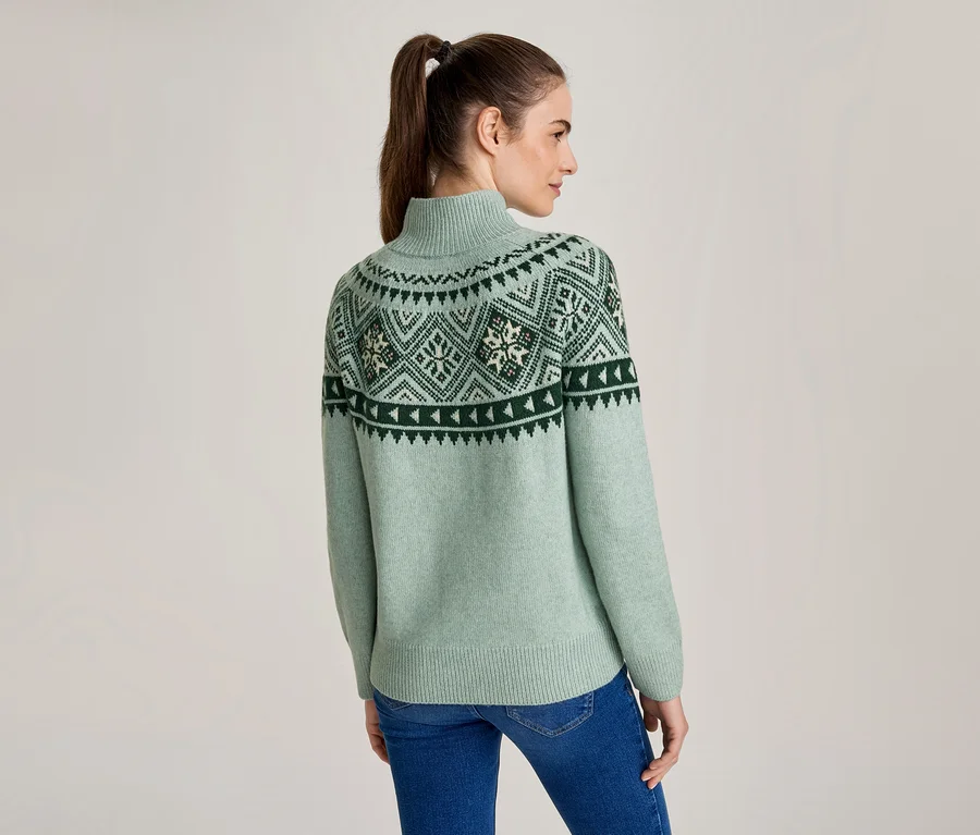 Frau von hinten in hellgrünem Rollkragenpullover mit dunkelgrünem und weißem Norwegermuster, dazu blaue Jeans.