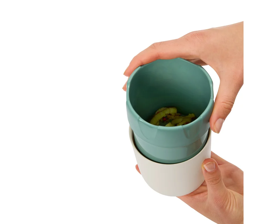 Hände halten zwei Becher, der obere ist türkis mit Inhalt, der untere ist weiß.