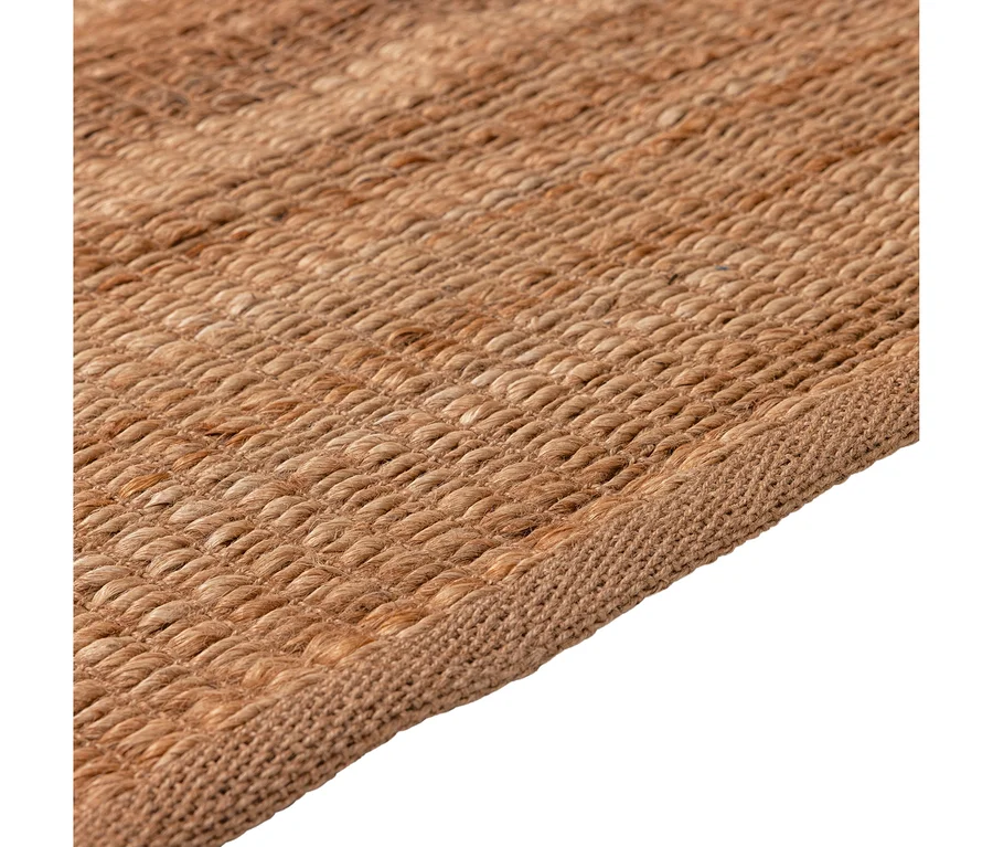 Nahaufnahme eines schräg liegenden, naturfarbenen, gewebten Teppichs mit ausgeprägter Textur und einer umrandeten Kante.