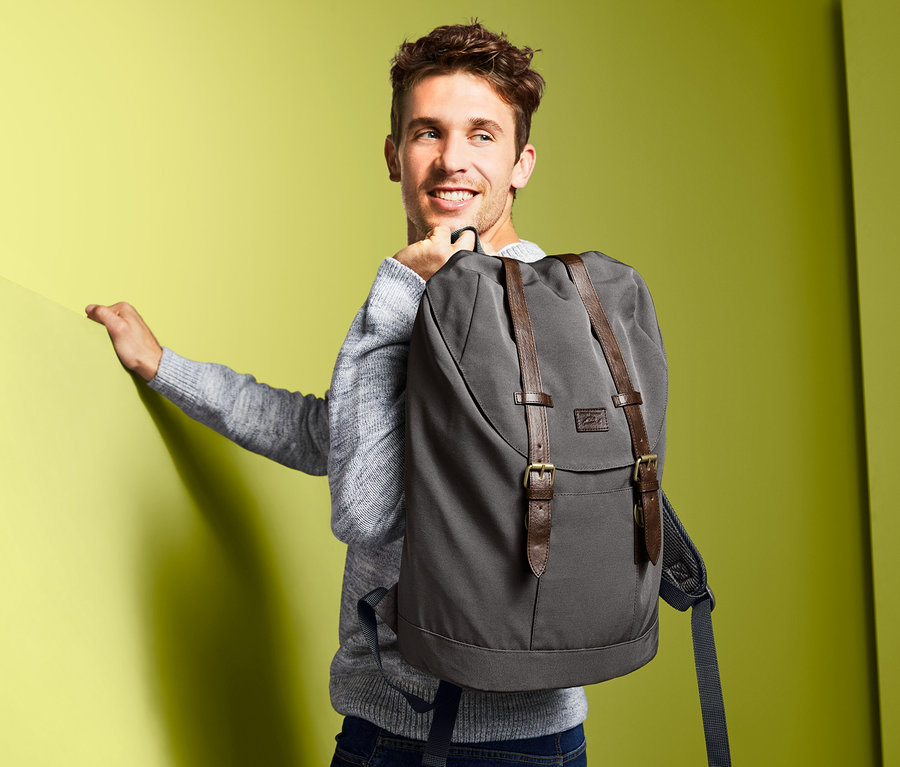 Mann mit Heritage-Rucksack über der Schulter posiert vor gelbem Hintergrund.