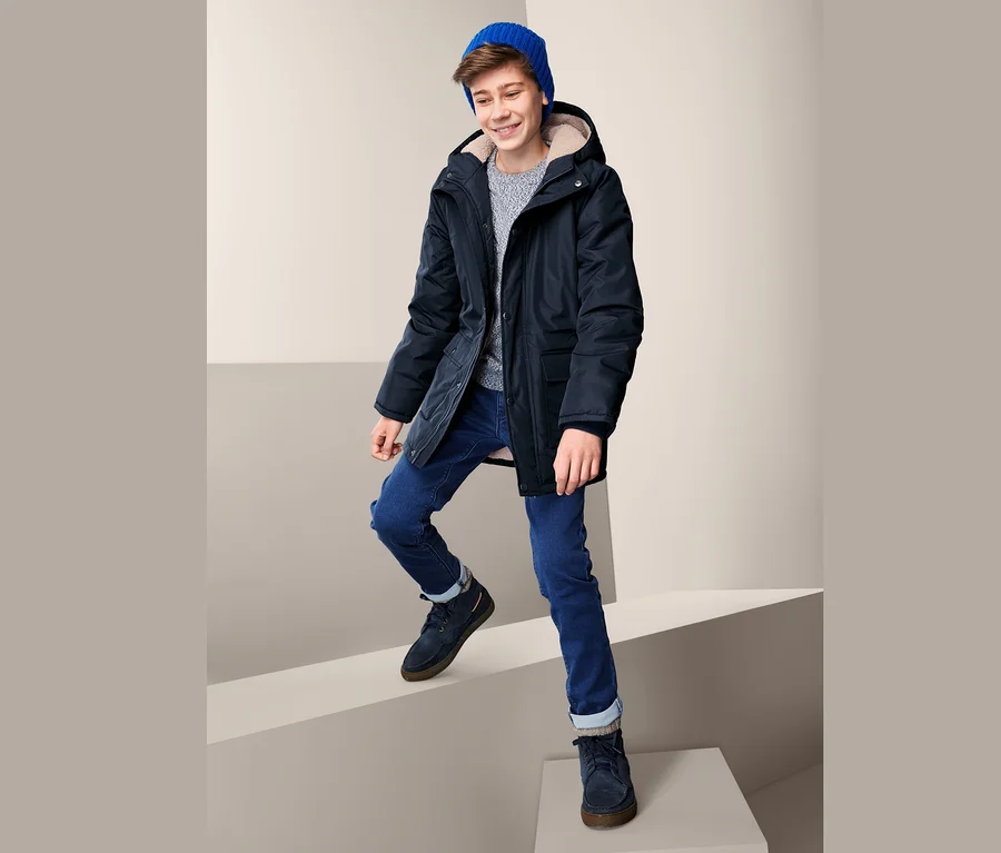 Ein junger Mann in Thermojacke und blauer Mütze steigt eine weiße Treppe hoch.