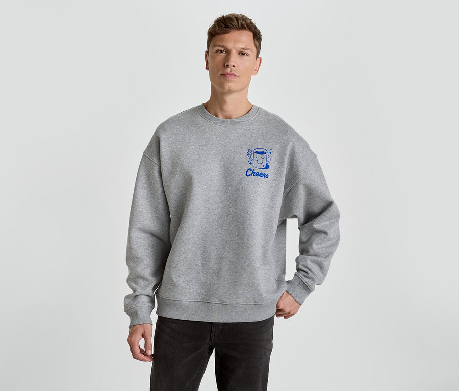 Mann trägt ein graues Sweatshirt mit dem blauen Aufdruck Cheers und einer Tasse darauf.