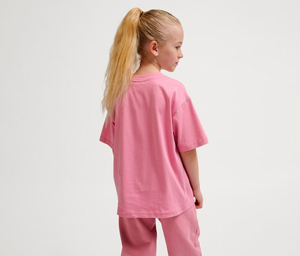 Mädchen von hinten, trägt ein rosafarbenes hummel hmUR loose T-Shirt »Bee« und eine passende Hose.