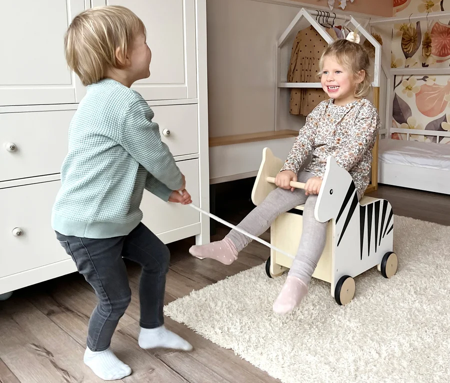 Junge zieht Mädchen, das auf small foot Spielzeugkiste Zebra »Wildlife« sitzt.