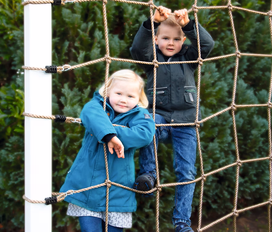 Zwei Kinder klettern auf einem small foot Kletternetz mit Achterhaken.