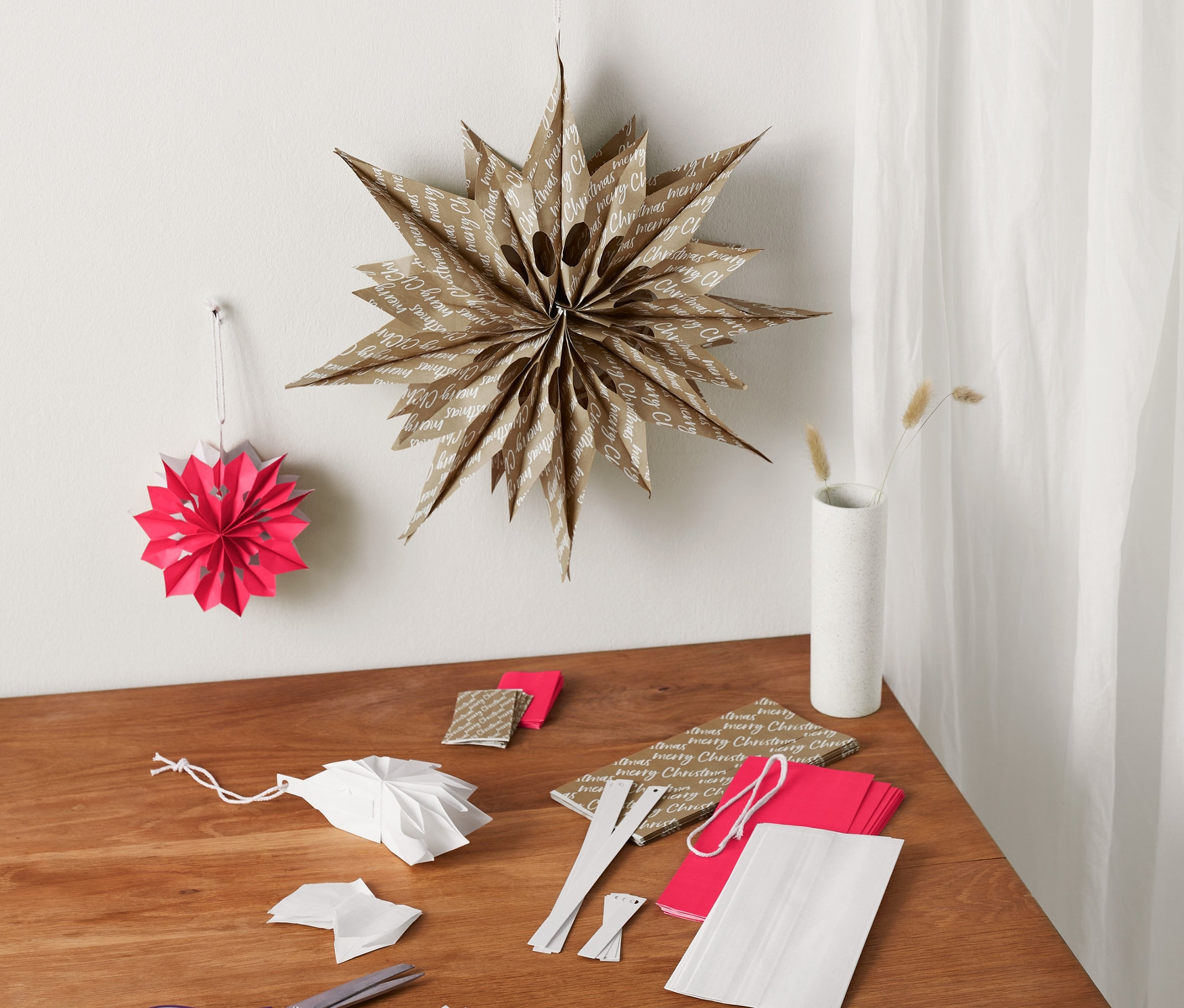 Auf einem Tisch liegt ein Papiertüten-Sterne-Bastel-Set und fertige Dekorationen.