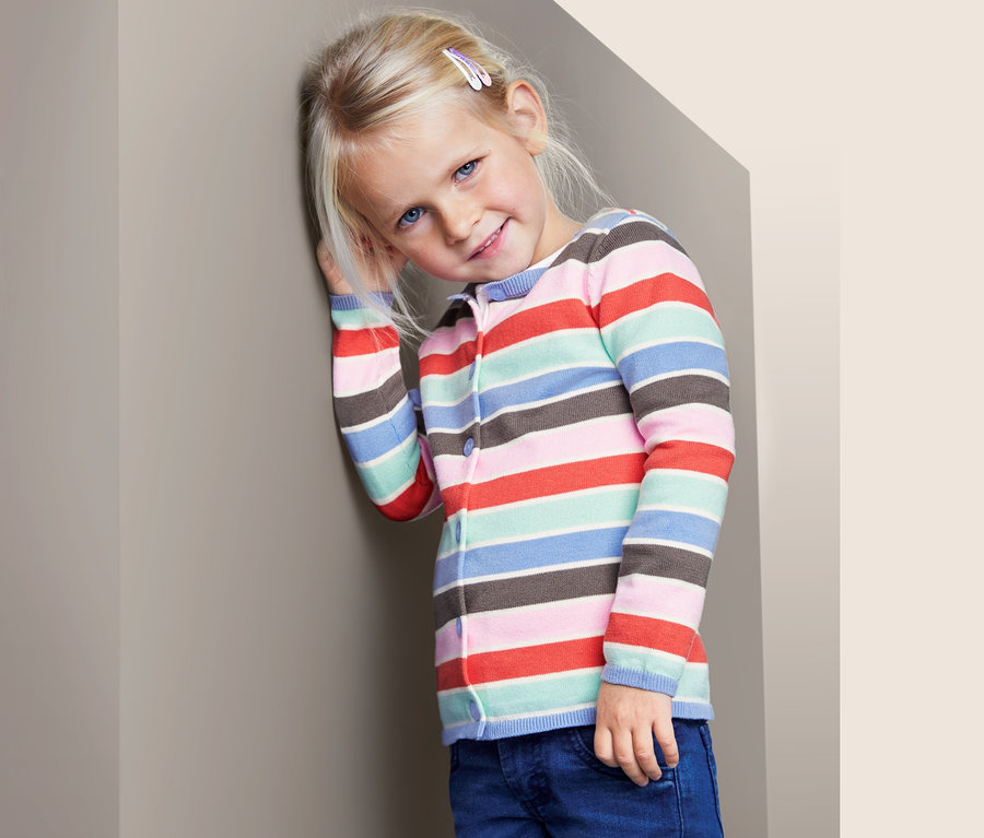 Mädchen lehnt an der Wand und trägt eine gestreifte Strickjacke.