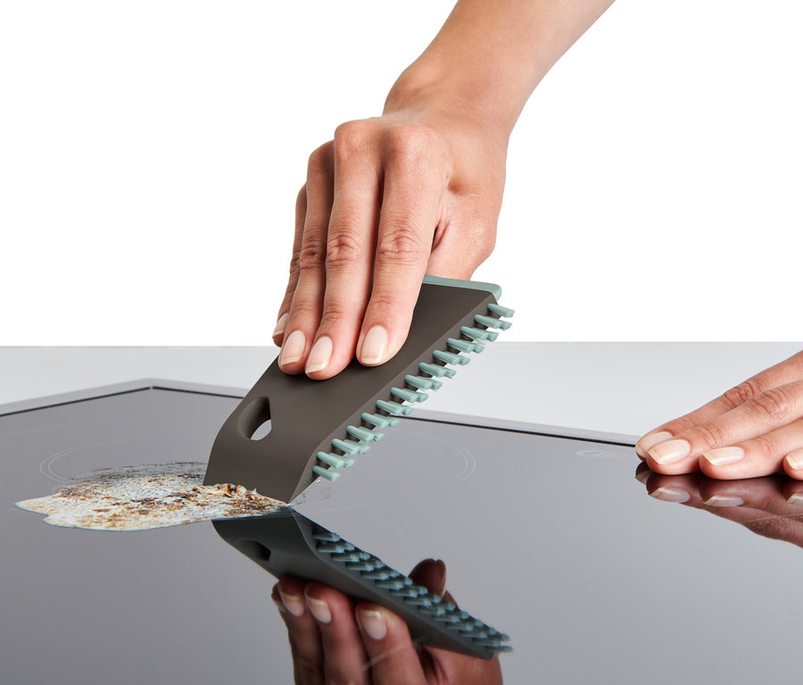 Eine Hand reinigt ein Glaskeramikkochfeld mit einer Universal-Küchenbürste.