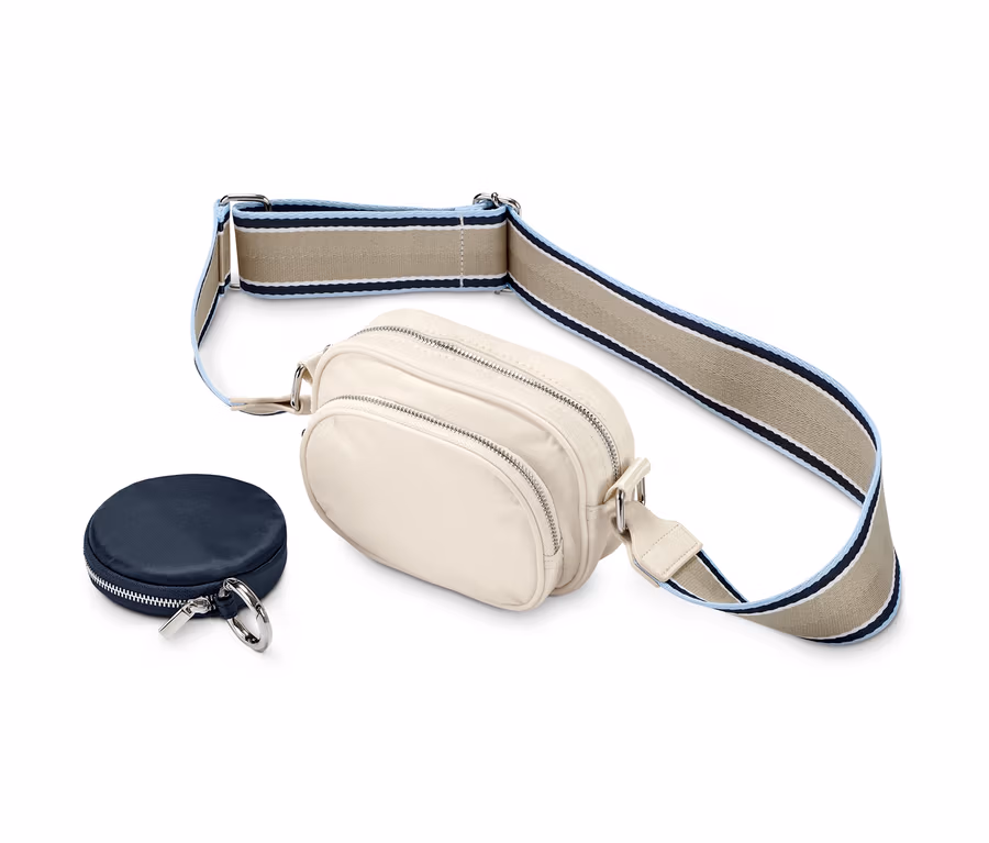 Eine beige Crossbody-Tasche mit Zierband und eine dunkelblaue Minitasche auf weißem Hintergrund.