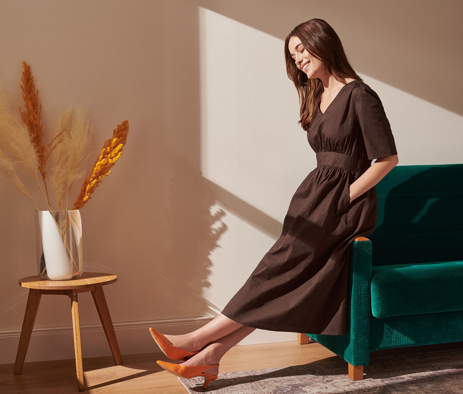 Frau sitzt auf einem grünen Sofa und trägt ein Midikleid.