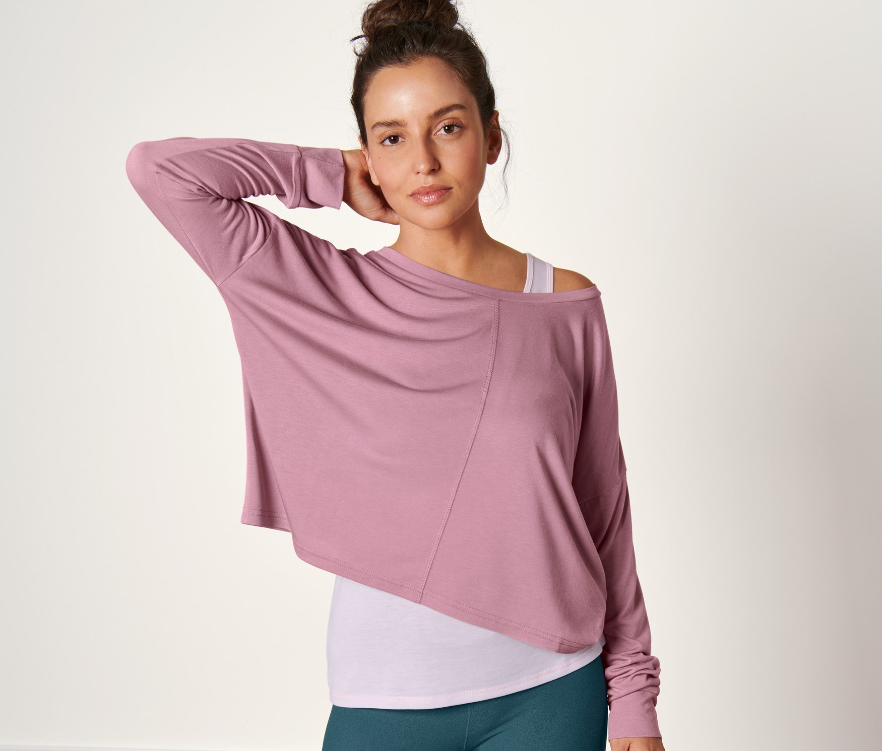 Frau posiert in einem rosa 2-in-1-Sportshirt und grünen Leggings.