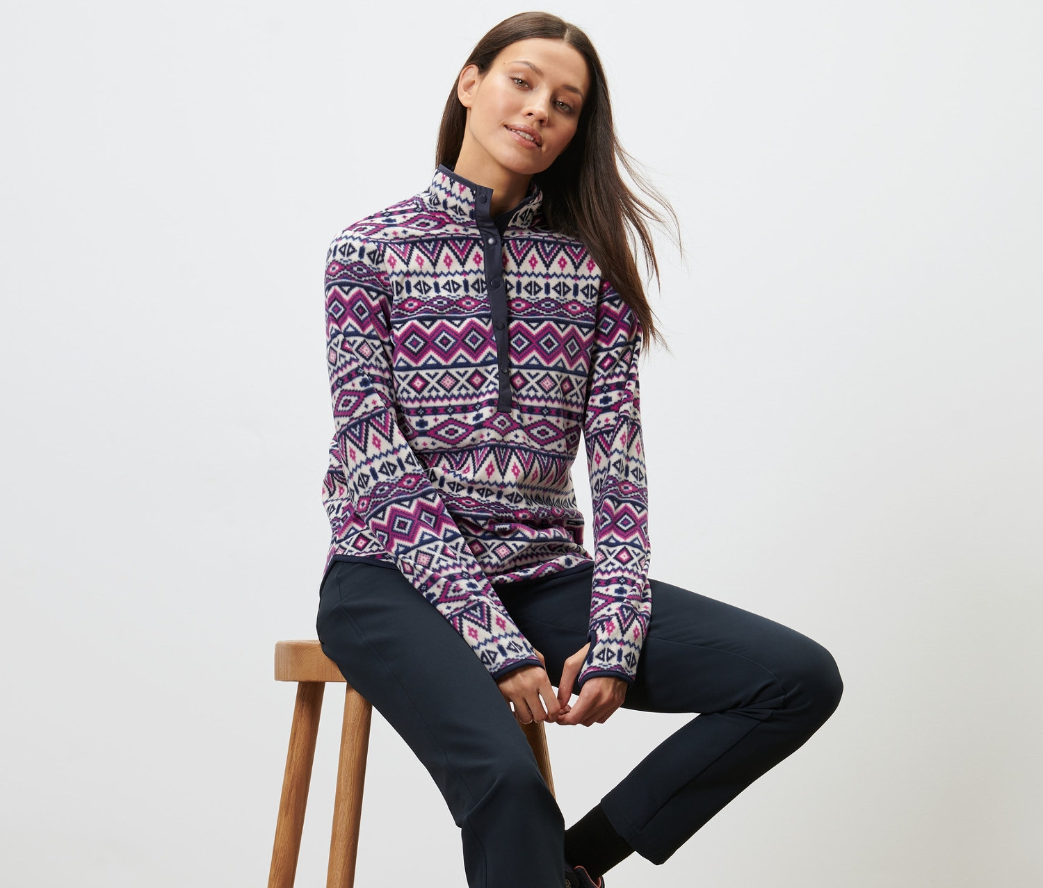 Frau sitzt auf einem Hocker und trägt einen Fleecepullover.